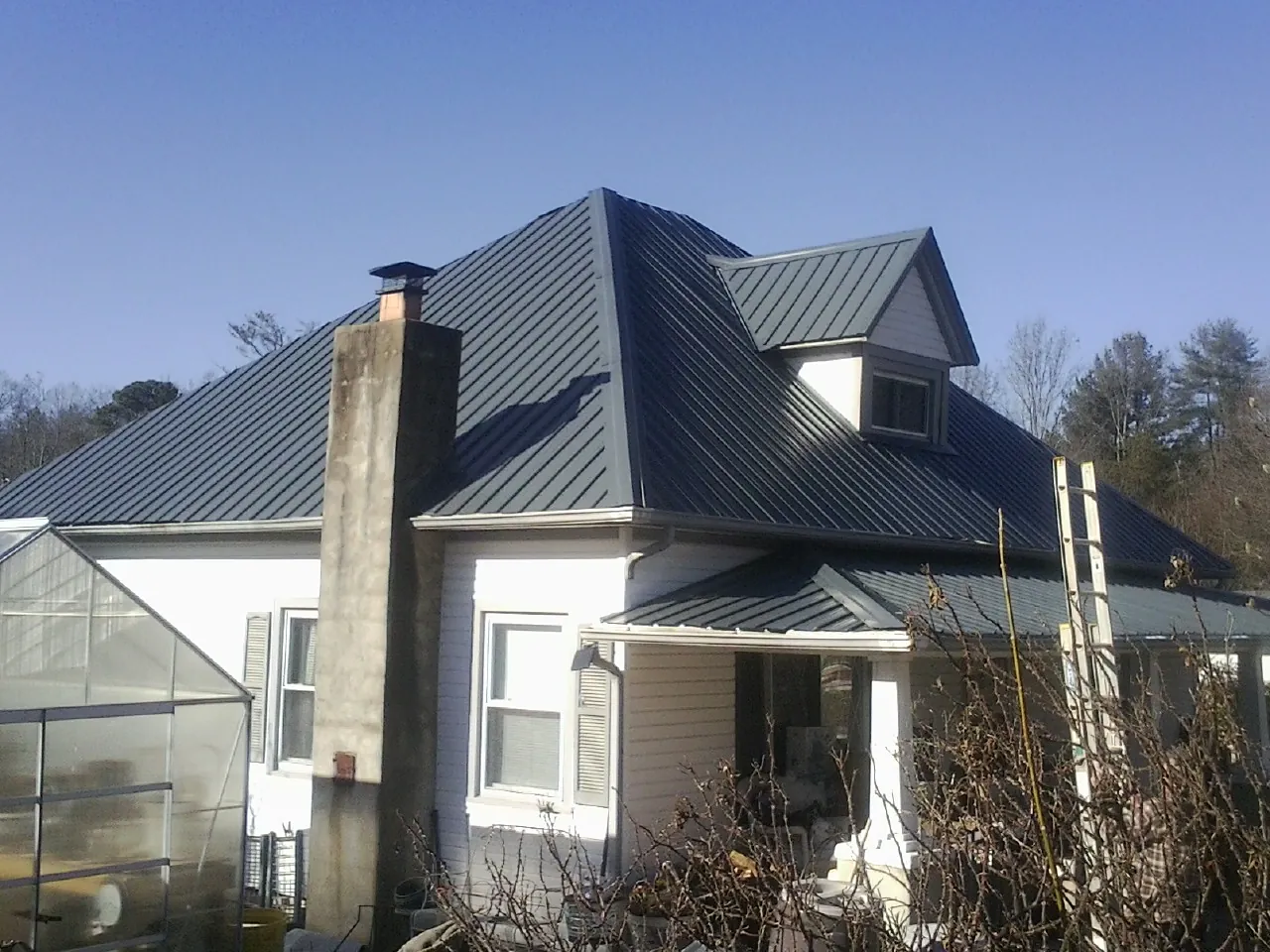 Dark blue standing seam metal roof on a white farmhouse with dormer — Slate & Tile Roof Repair by Roofing Brothers in Hardy