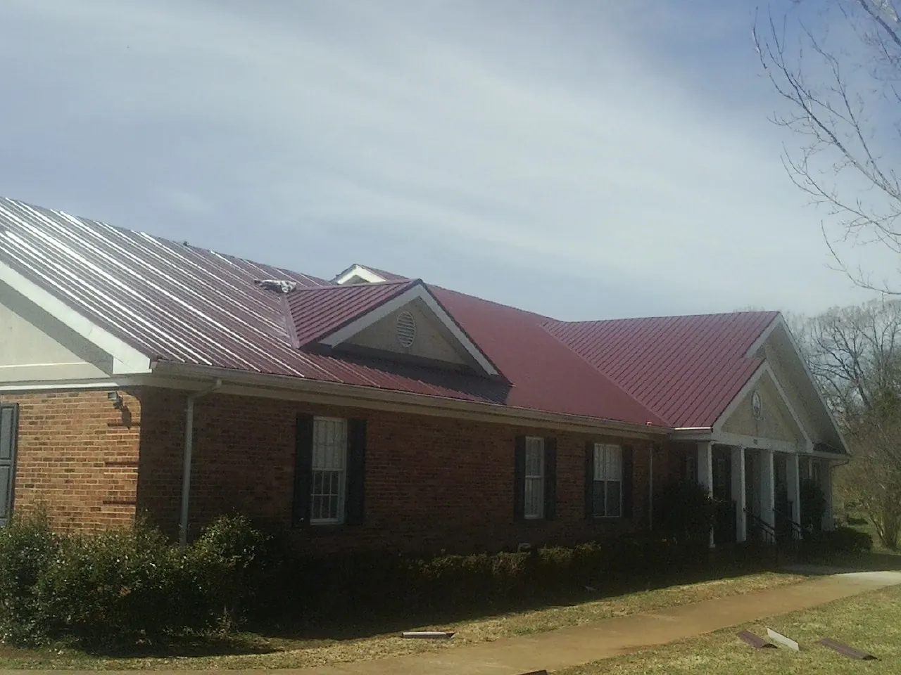 Red metal roof with gabled entries on a long brick building, from a Hail Damage Roof Repair job in Hardy