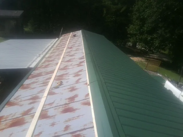 Old rusted panels beside newly installed green metal roofing — Wind Damage Roof Repair by Roofing Brothers in Hardy