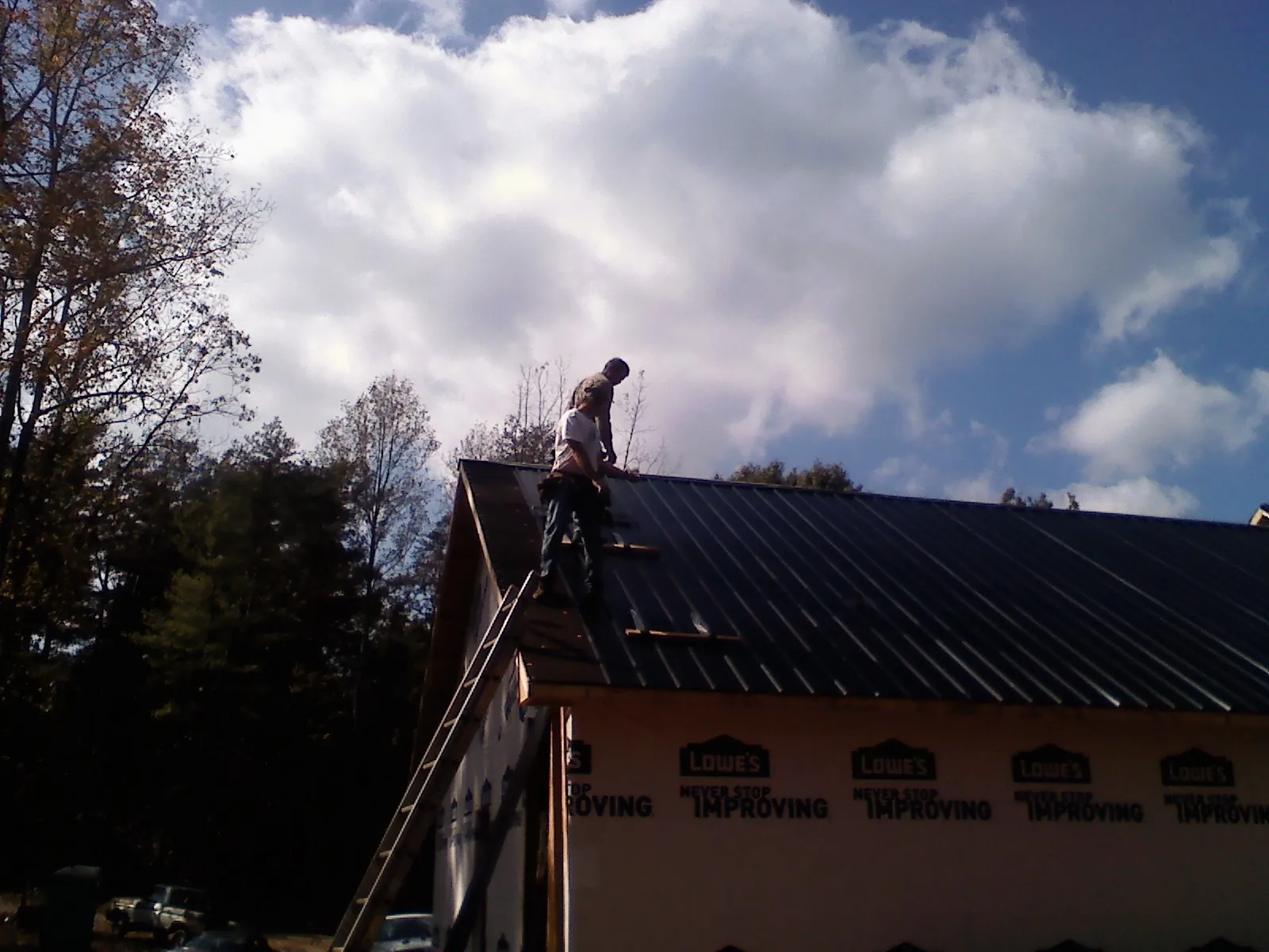 Roofer fastening dark metal panels high against a cloudy sky, from a Roof Inspection job in Hardy